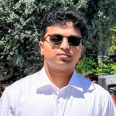Dayakshin wearing sunglasses and a white collared shirt outdoors with trees in the background.