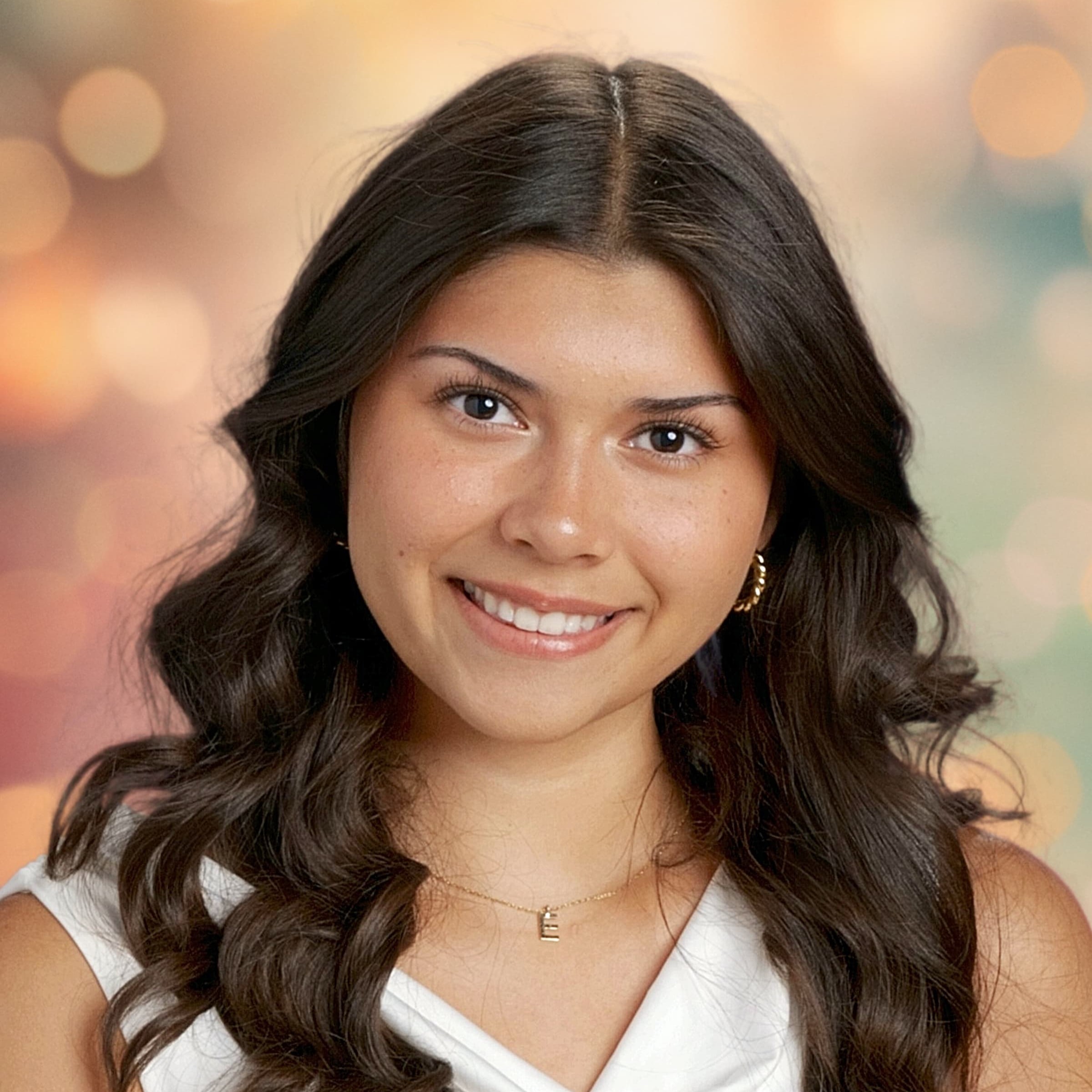 Close-up portrait of Eden with long wavy dark hair, wearing gold hoop earrings and a necklace, against a softly blurred bokeh background.