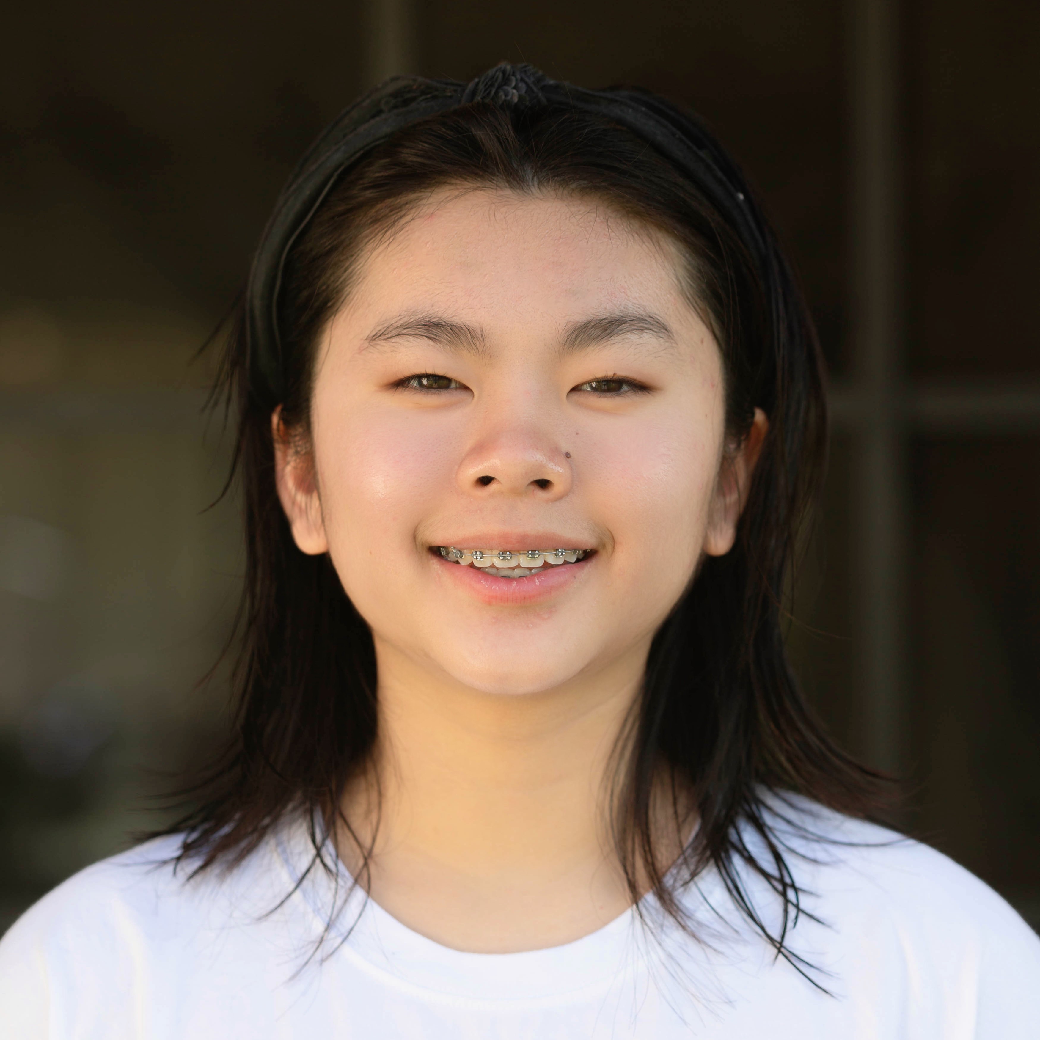 Close-up portrait of Flora with dark hair wearing braces and a white shirt.