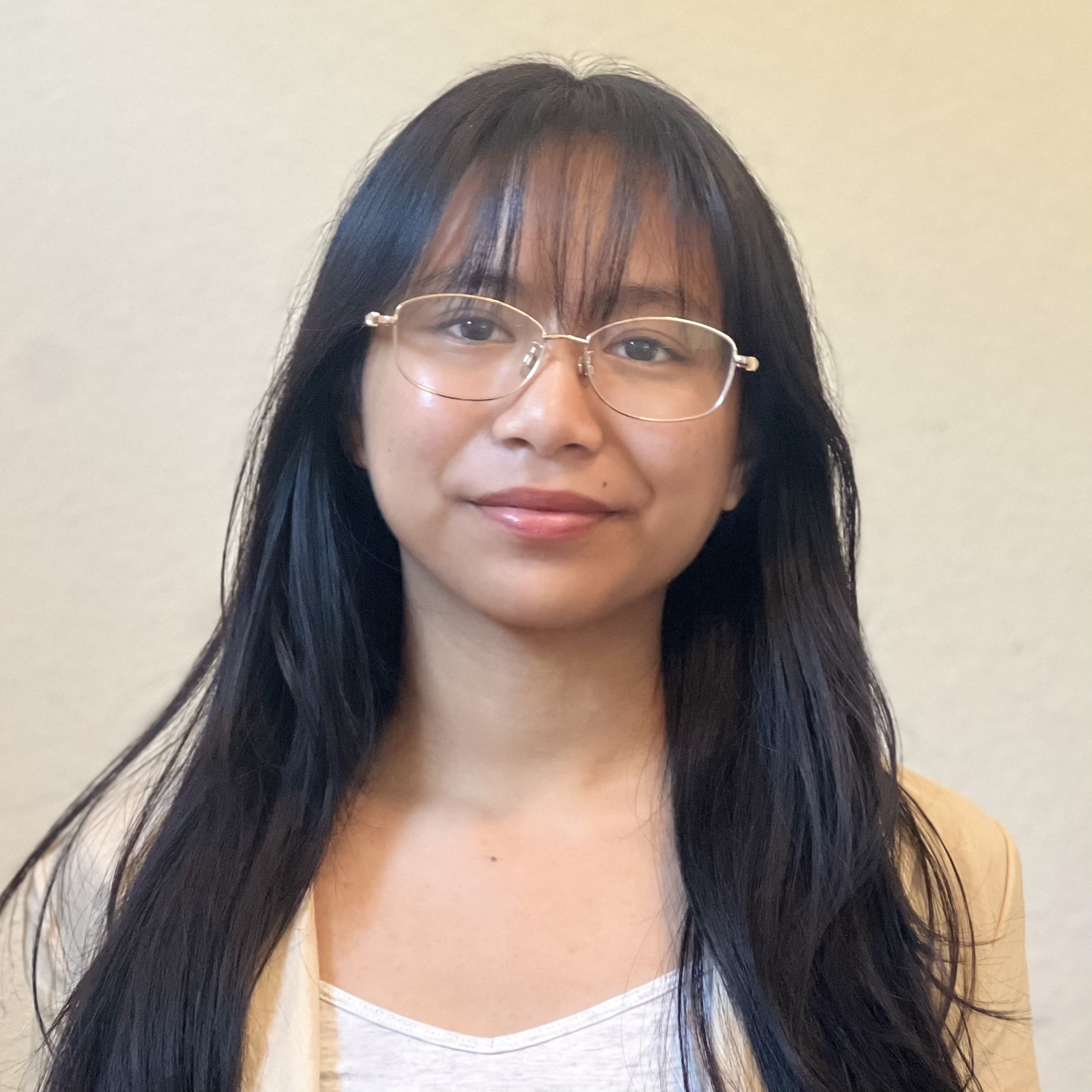 Close-up portrait of Jesstel with long dark hair and bangs, wearing gold-rimmed glasses and smiling slightly against a plain background.