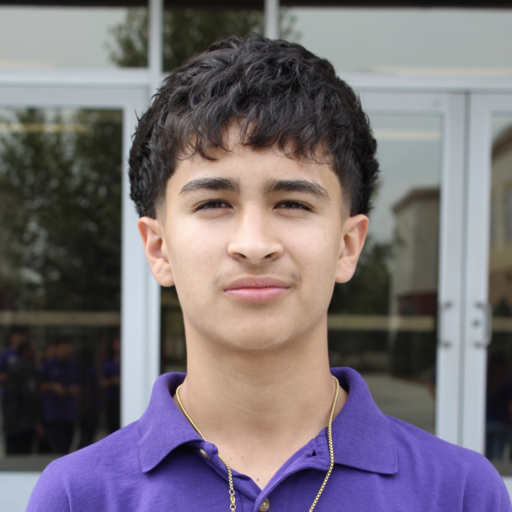 Close-up portrait of Jesus in a purple polo shirt standing in front of glass doors.