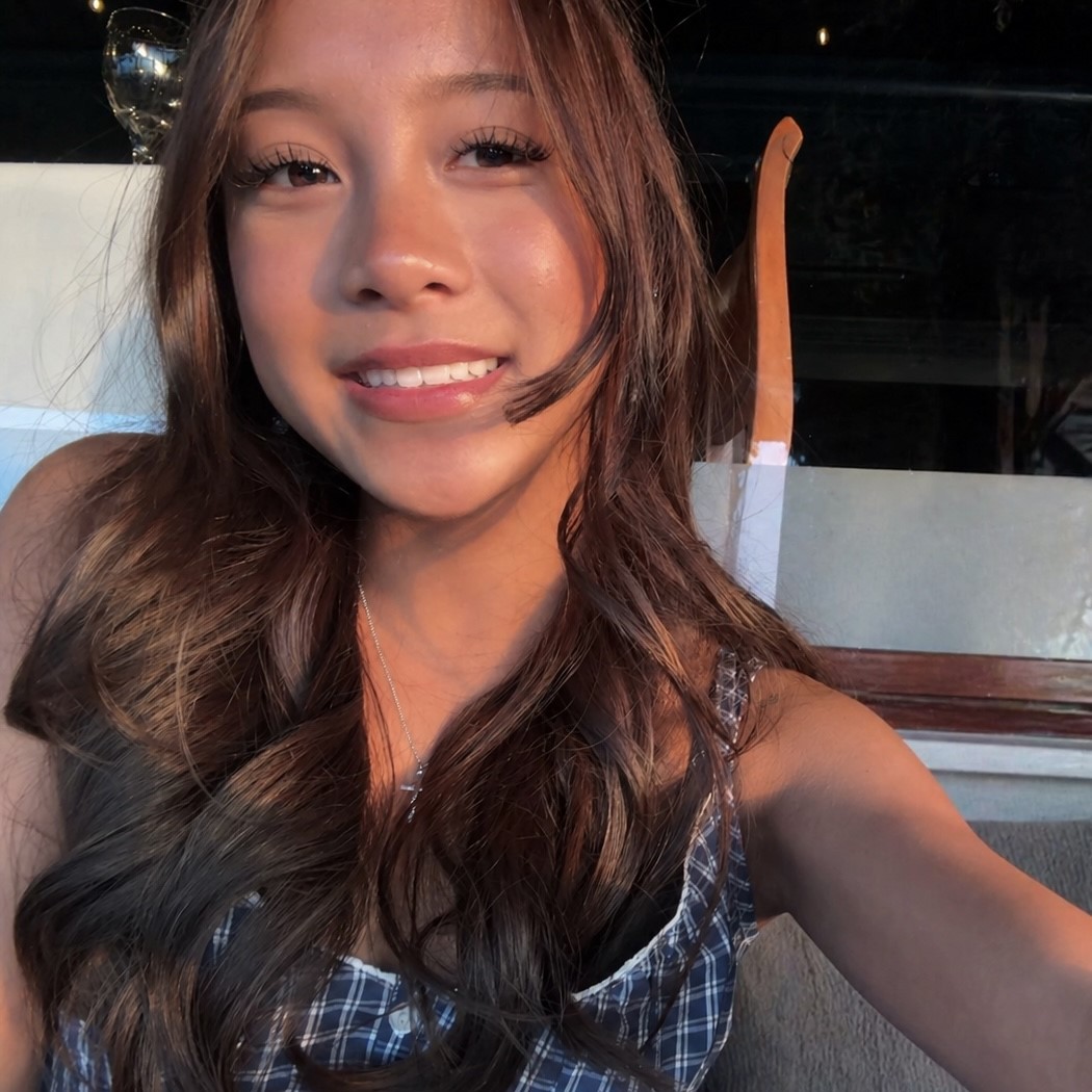 Close-up selfie of Khloe with long wavy hair in warm sunlight, indoors near a window.
