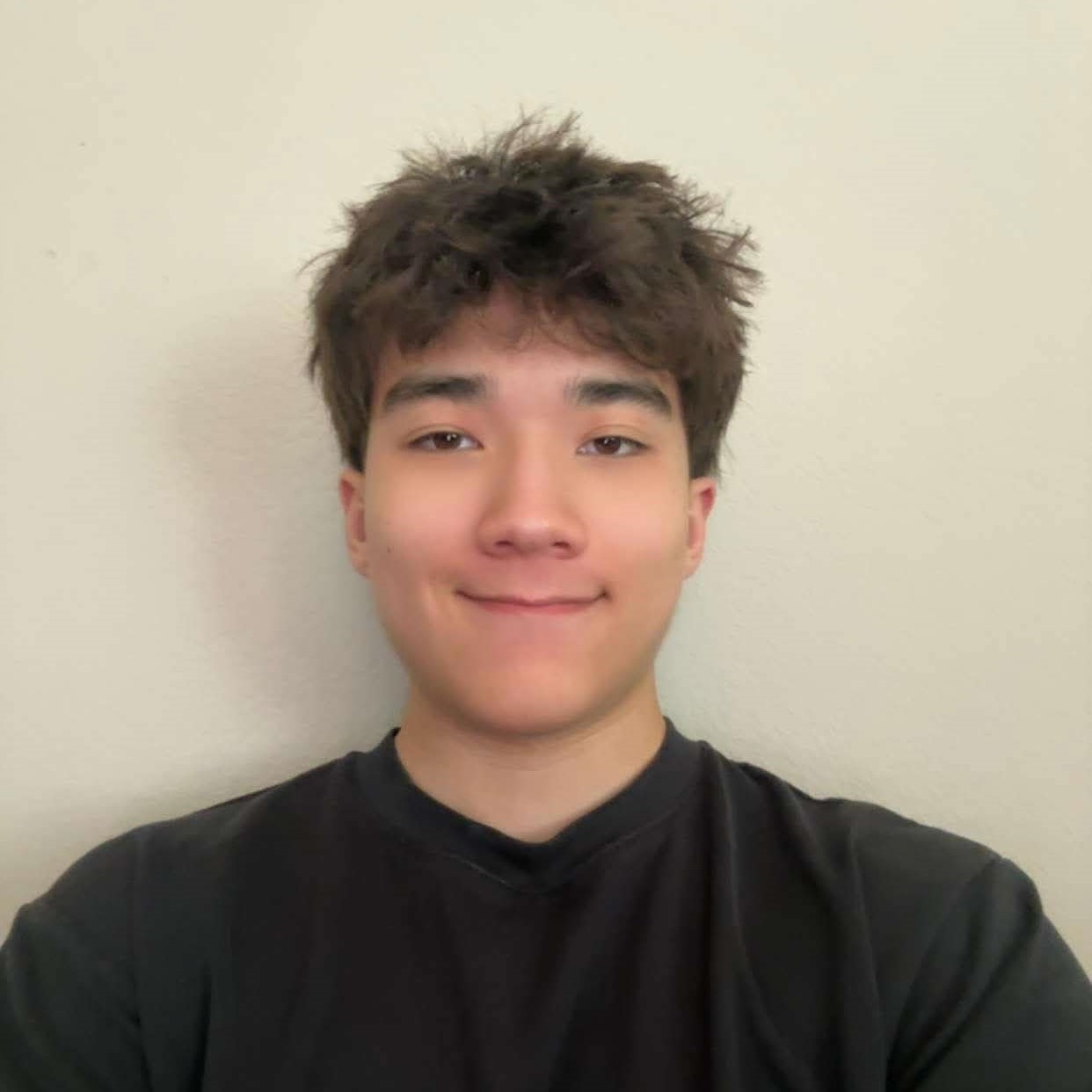 Portrait of Meridian with tousled dark hair wearing a black shirt against a plain light-colored wall.
