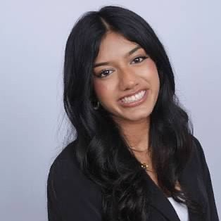 Headshot of Shivani smiling with long dark hair against a light gray background.
