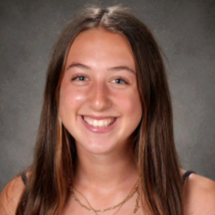 Smiling Siena with long brown hair in a studio headshot against a gray background.