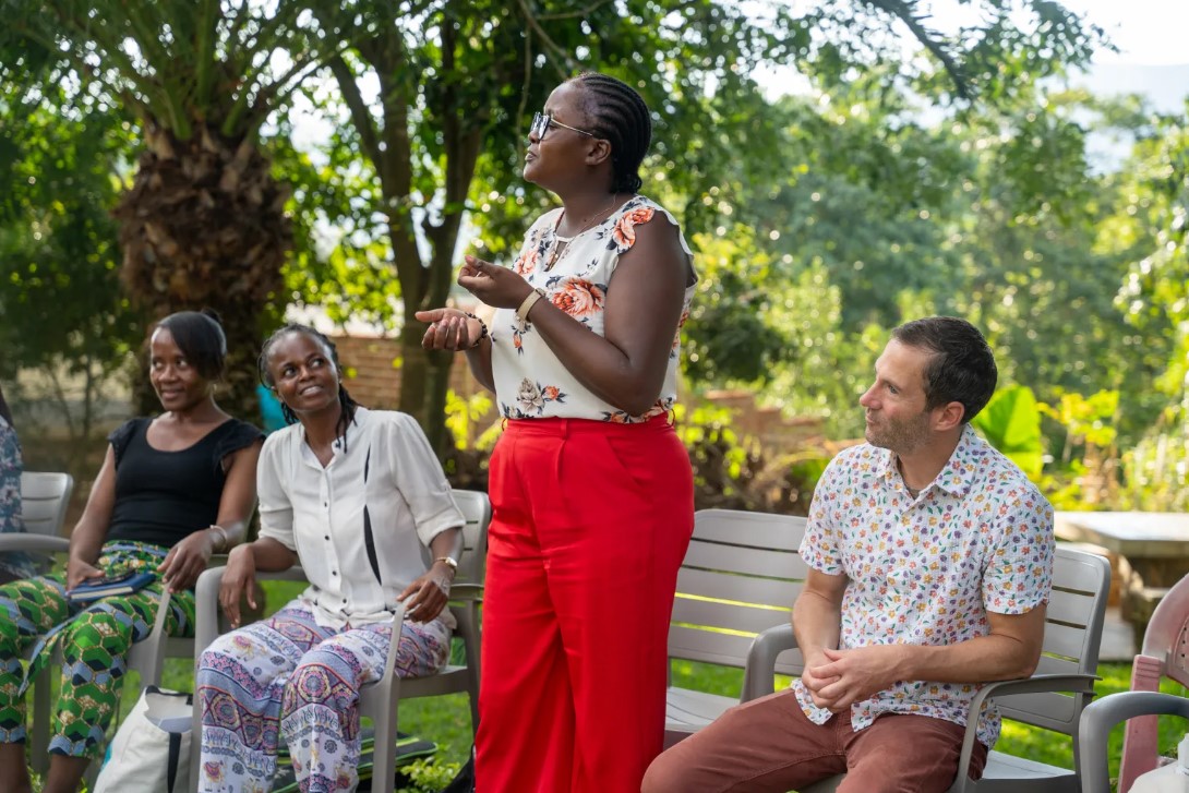 Woman speaking to a small group seated outdoors under trees in Malawi.