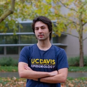 Headshot of Alexandre Rico wearing a UC Davis Epidemiology t shirt and standing in front of trees