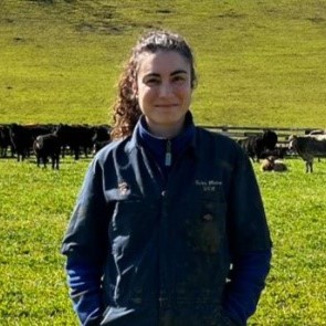 Photo of Ana da Silva Oliveira standing in a grass field with cows behind her
